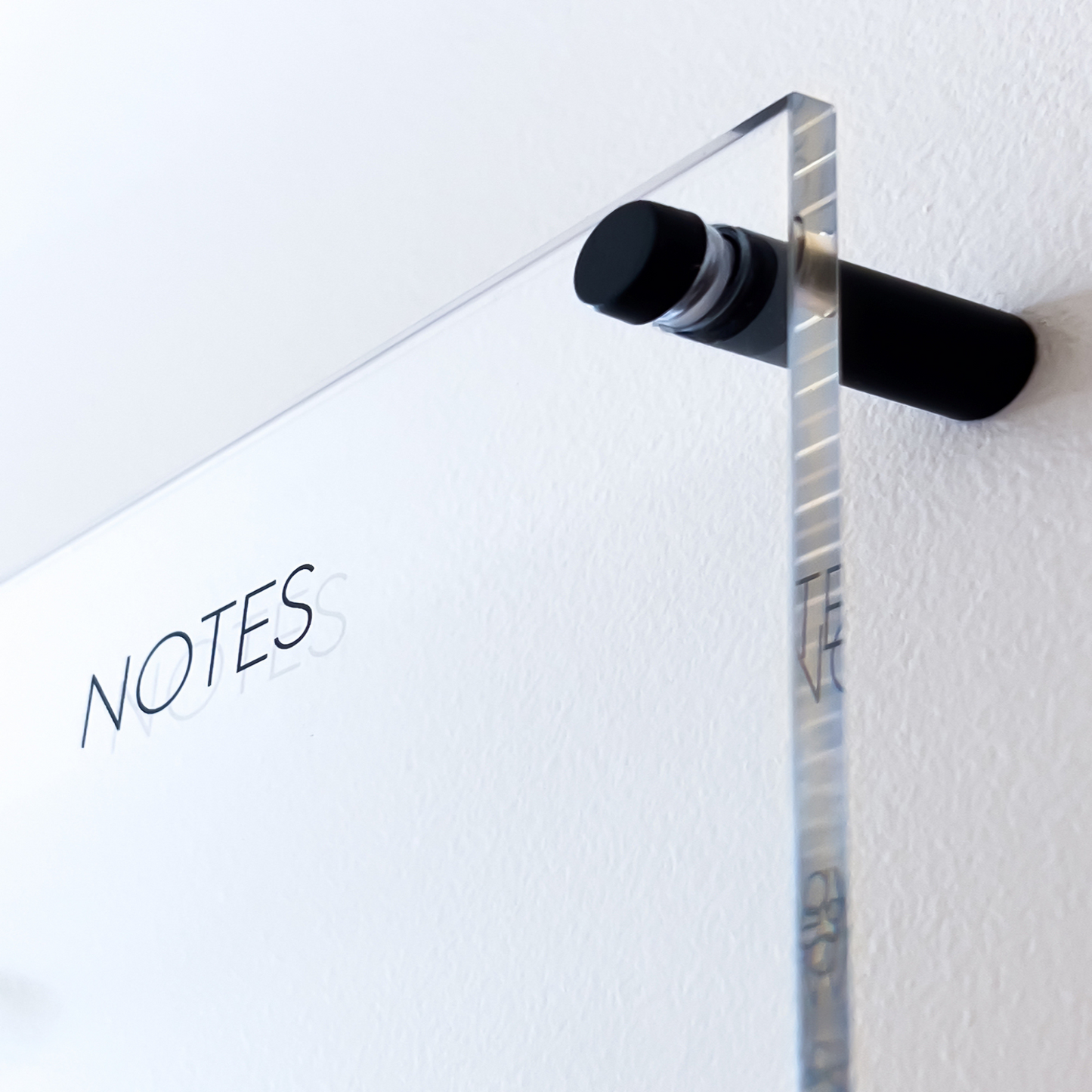 Close-up view of the Lux Navia wall-mounted clear acrylic planner, featuring the word 'NOTES' and a sleek black mounting post for a modern and minimalist look.